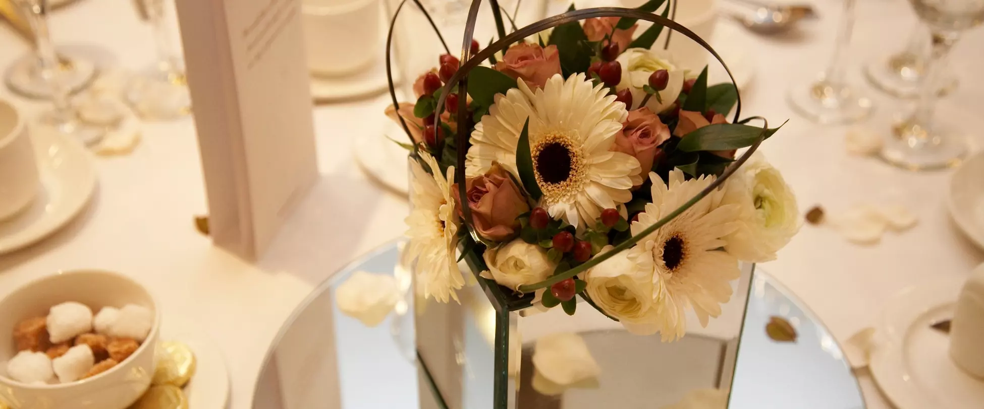 An arrangement of white and pink flowers in a mirrored cube sat in the middle of a dressed table..